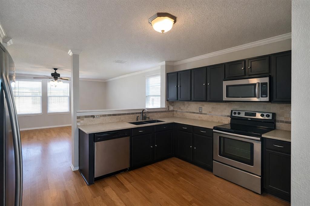 1621 Carolina Ridge Way Fort Worth, TX 76247 - Photo 3 of 7 Kitchen with stainless steel appliances, light countertops, dark cabinetry, ornamental molding, and light wood-type flooring