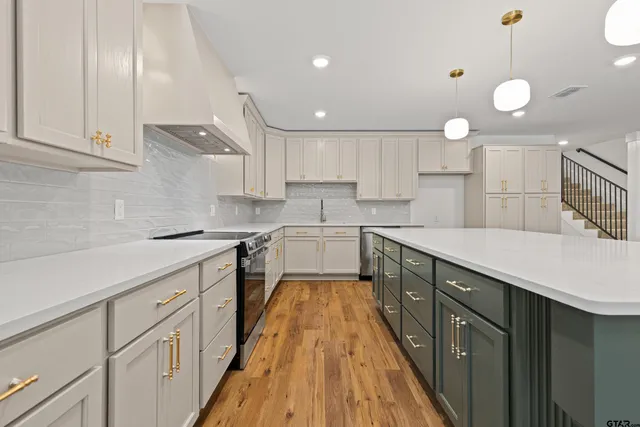 a large kitchen with kitchen island granite countertop a stove a sink a refrigerator and white cabinets with wooden floor