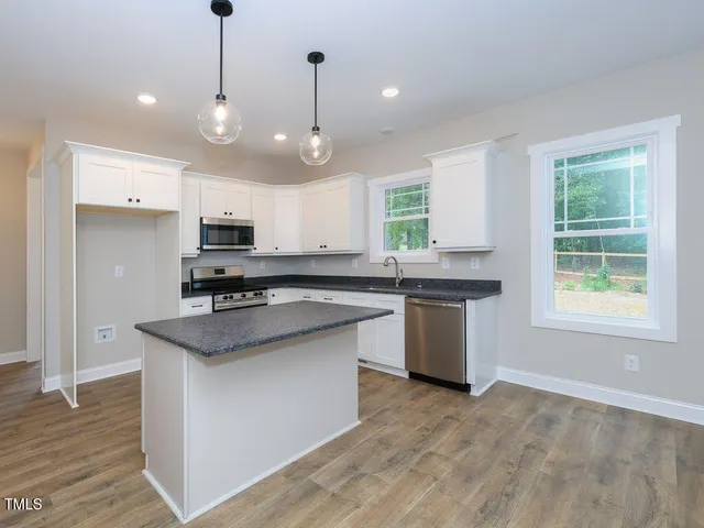 a kitchen with stainless steel appliances granite countertop a sink a stove a refrigerator and island with wooden floor