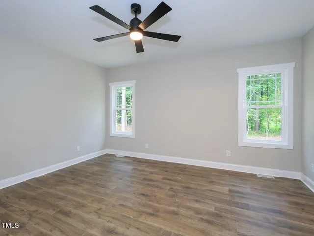an empty room with wooden floor ceiling fan and windows
