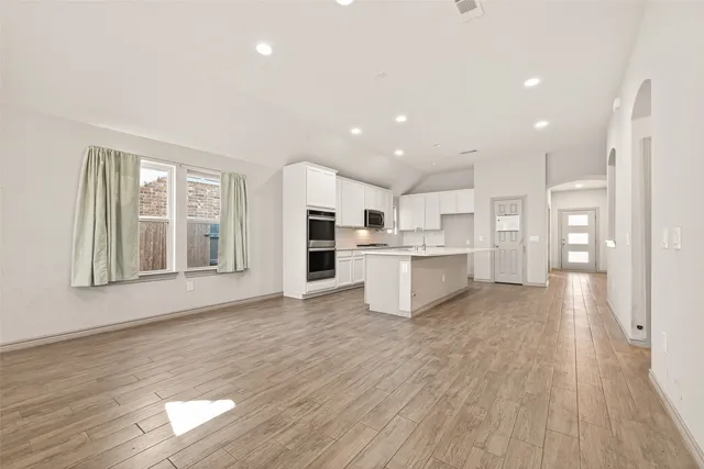 a kitchen with stainless steel appliances granite countertop a stove top oven a sink a refrigerator white cabinets and wooden floor