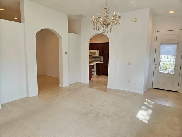 an empty room with chandelier fan and kitchen view