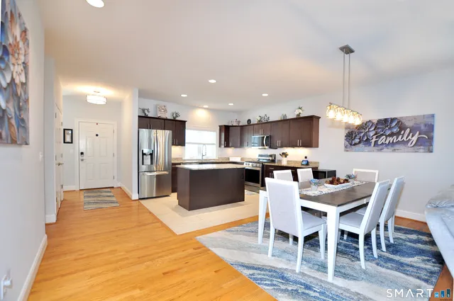 a kitchen with stainless steel appliances kitchen island granite countertop a dining table chairs sink and white cabinets