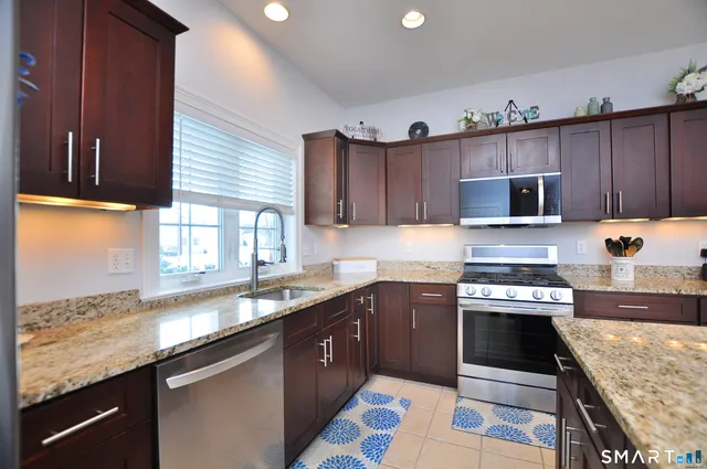 a kitchen with granite countertop stainless steel appliances a sink a stove a microwave cabinets and a counter top space