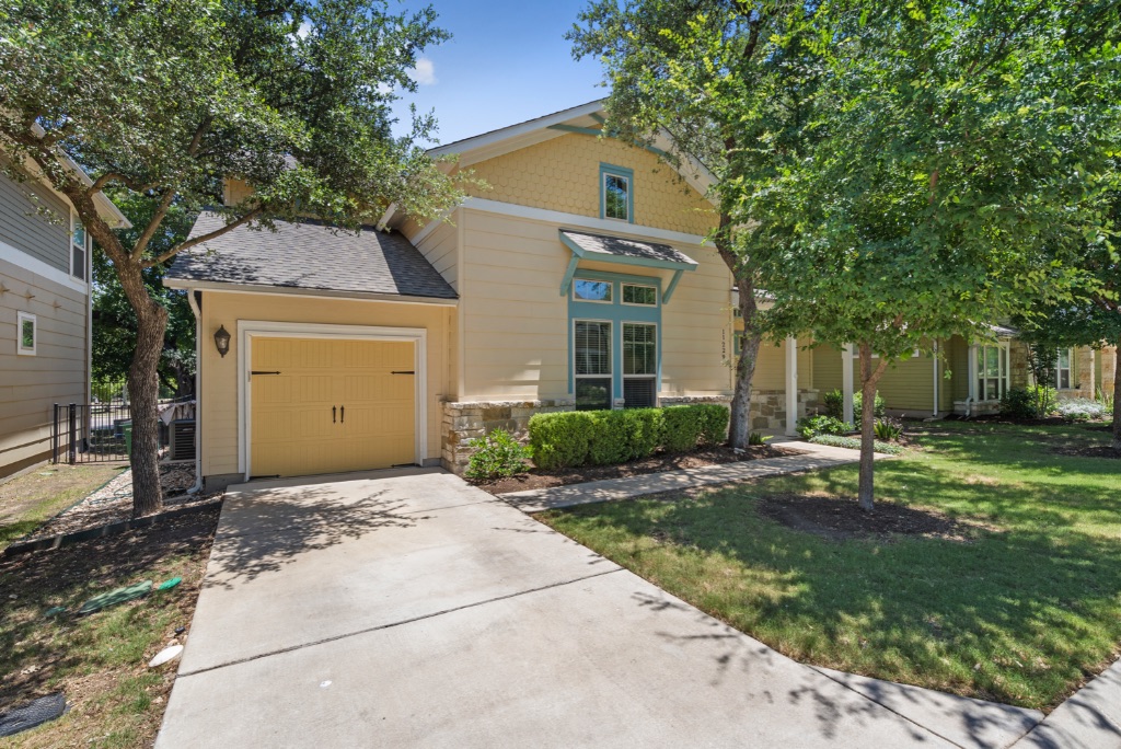 View of front of home featuring a garage, driveway, a front lawn, stone siding, and roof with shingles