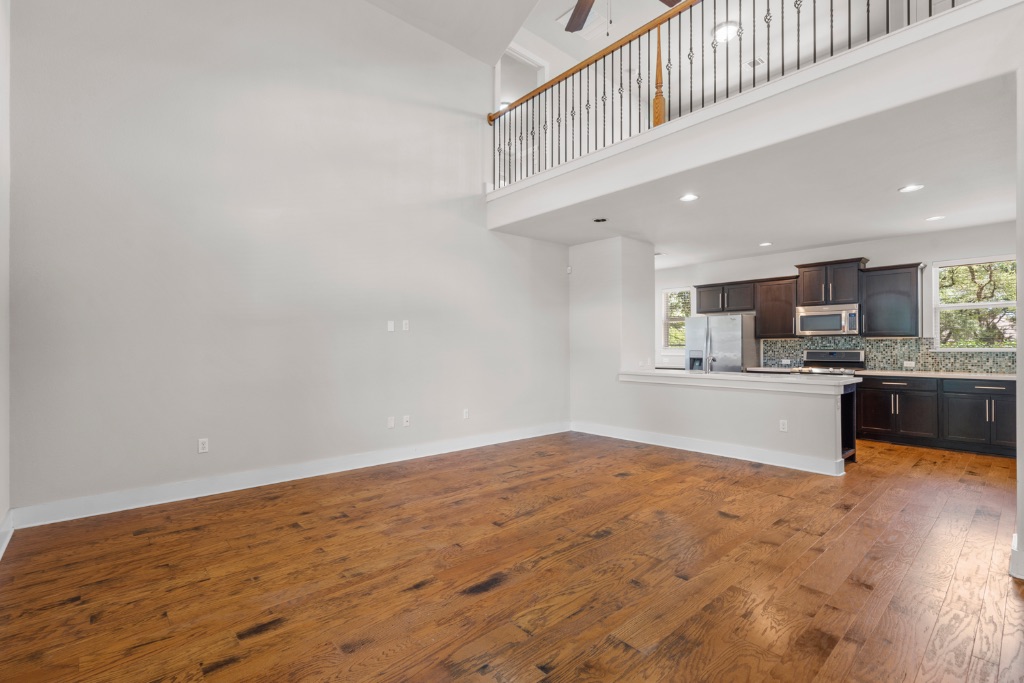 11229 Avery Station Loop, Unit 36 Austin, TX 78717 - Photo 5 of 37 Unfurnished living room with healthy amount of natural light, dark wood-type flooring, a high ceiling, a ceiling fan, and recessed lighting