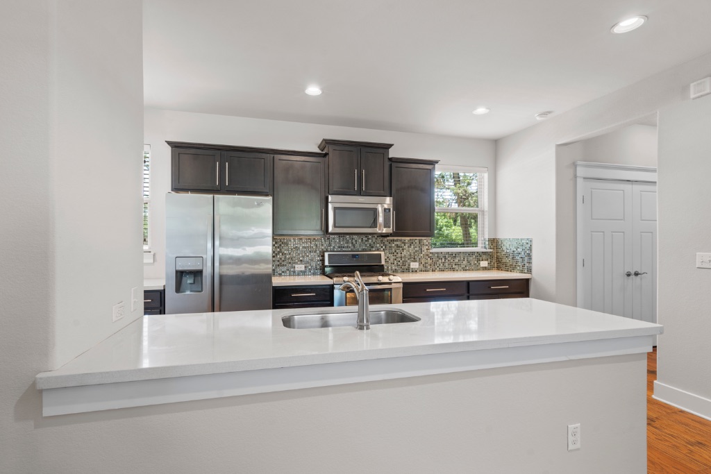 11229 Avery Station Loop, Unit 36 Austin, TX 78717 - Photo 8 of 37 Kitchen with stainless steel appliances, a peninsula, dark wood finish cabinetry, backsplash, and light stone countertops