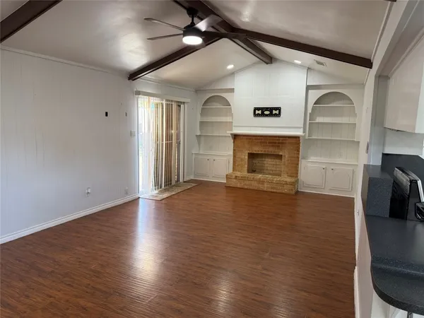 an empty room with wooden floor fireplace and windows