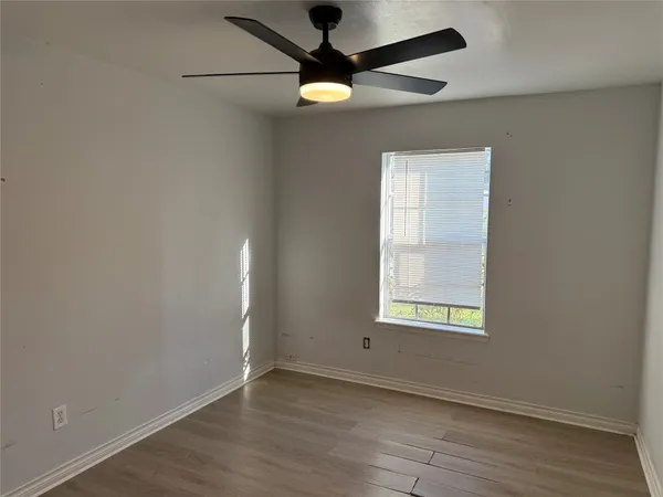an empty room with wooden floor chandelier fan and windows