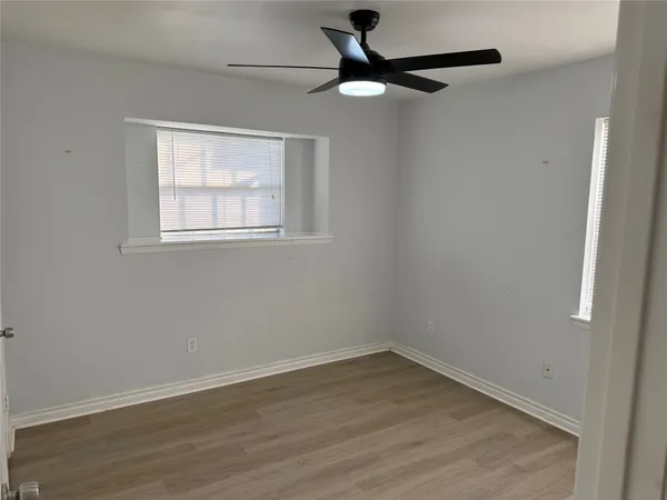 an empty room with wooden floor fan and windows