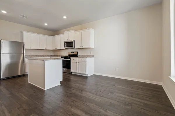a kitchen with stainless steel appliances granite countertop a stove top oven a sink a refrigerator and white cabinets with wooden floor
