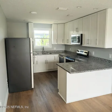 a kitchen with stainless steel appliances granite countertop a refrigerator a stove a sink and white cabinets with wooden floor