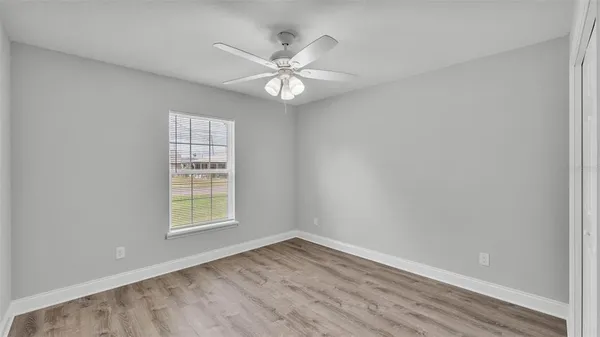 an empty room with wooden floor fan and windows