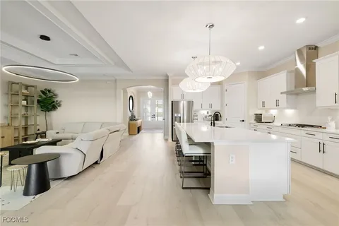 a large living room with stainless steel appliances kitchen island granite countertop a large couches a fireplace and a chandelier with kitchen view