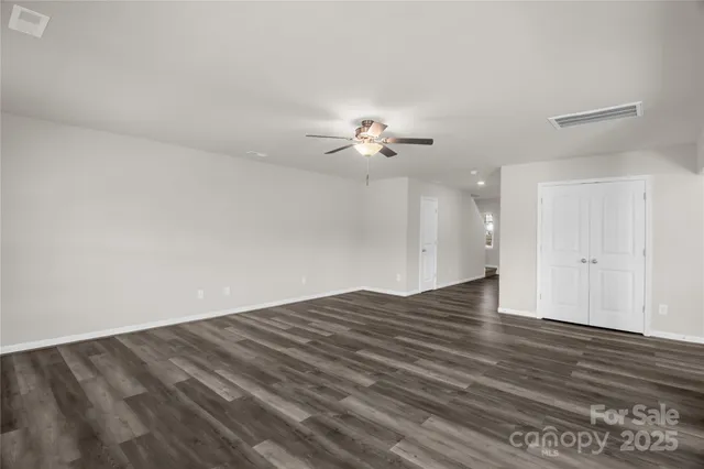an empty room with wooden floor chandelier fan and windows