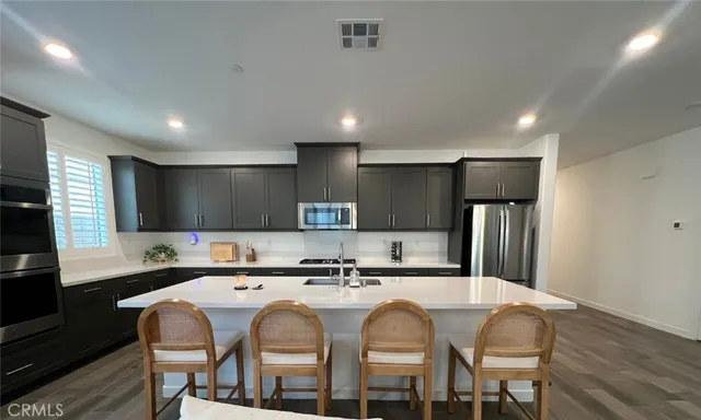 a kitchen with stainless steel appliances granite countertop a sink a stove a refrigerator and island with wooden floor