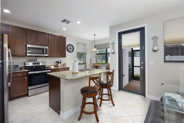 a kitchen with stainless steel appliances kitchen island granite countertop a stove a sink a refrigerator and chairs