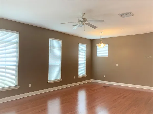 an empty room with wooden floor fan and windows