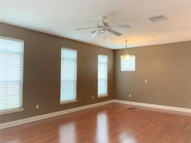 an empty room with wooden floor fan and windows