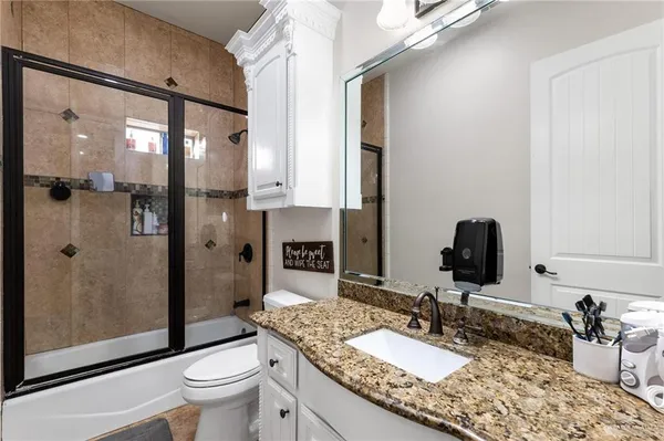 a bathroom with a granite countertop sink a toilet a mirror and shower
