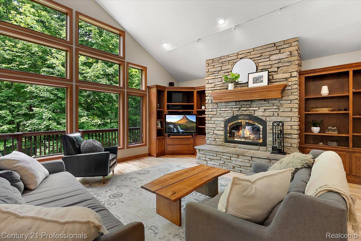9867 Rainbow Ridge Drive Schoolcraft, MI 49087 - Photo 19 of 82 Vaulted ceiling living area featuring a stone fireplace with wood mantel, built-in shelving, wood-finish flooring, and expansive windows
