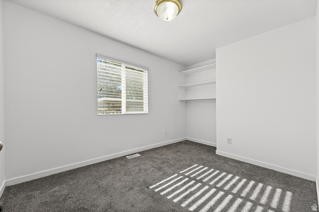 5525 Hampton Way Stansbury Park, UT 84074 - Photo 10 of 35 Neutral-toned room featuring a single window with blinds, carpet flooring, a flush-mount ceiling light fixture, and built-in shelving