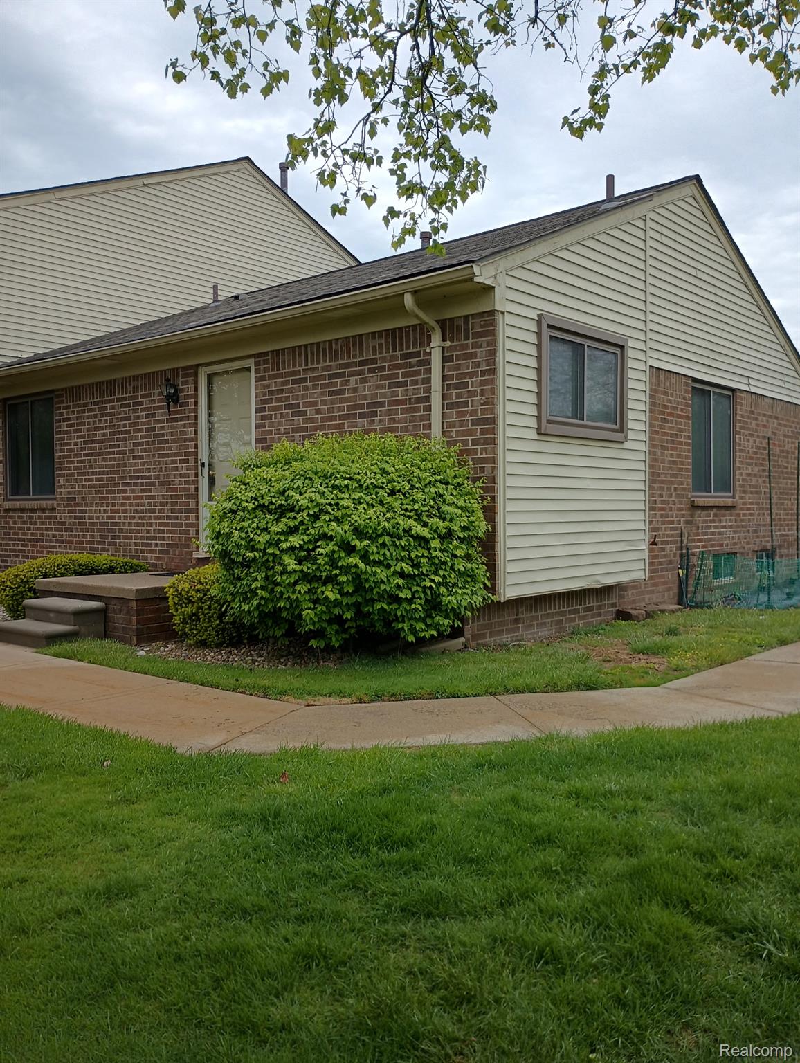 Brick and siding exterior featuring a front entry door with storm door, flanked by a manicured shrub