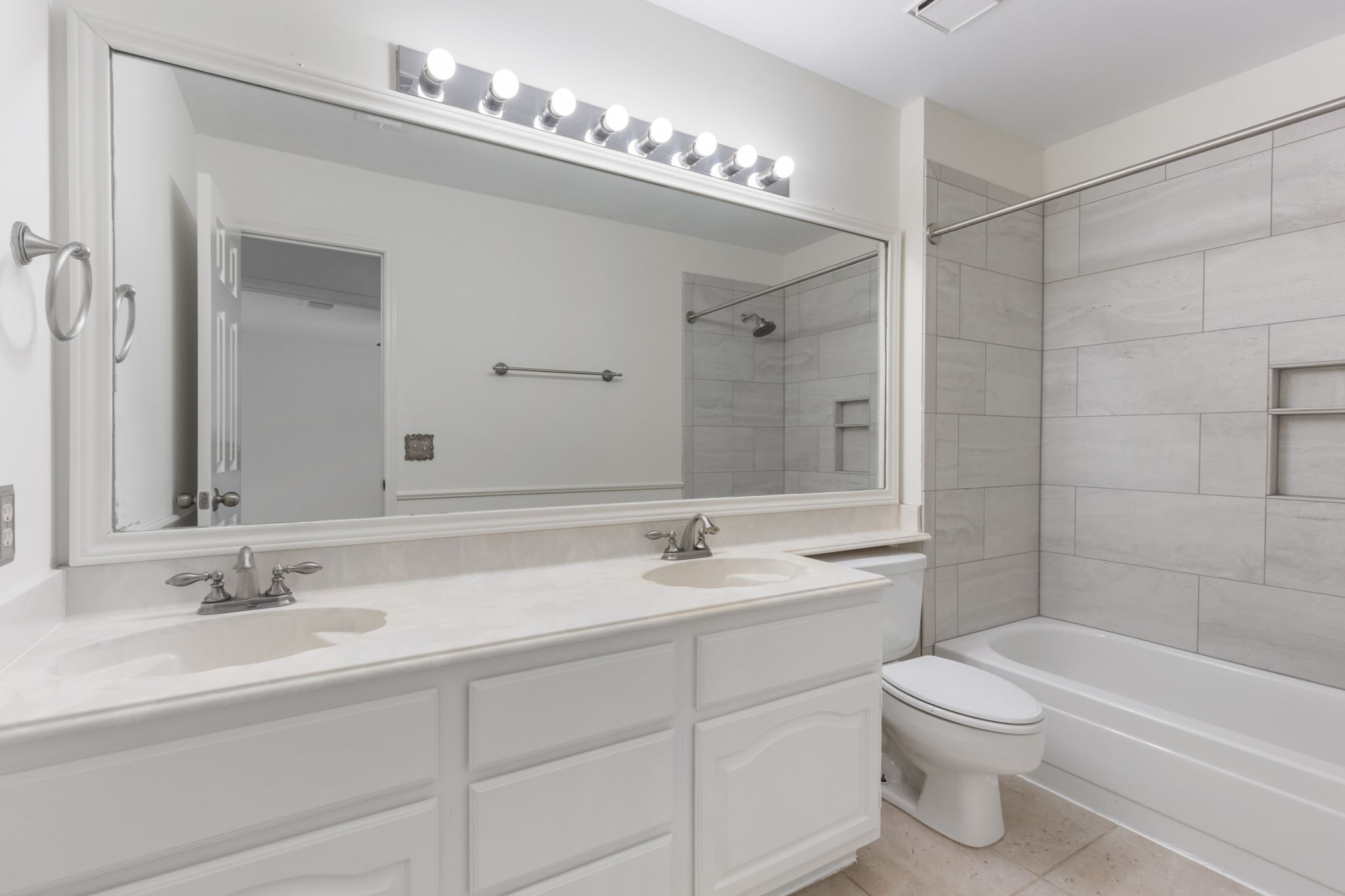 59 Fire Flicker Place Spring, TX 77381 - Photo 27 of 37 This bathroom features a clean design with a double vanity, large mirror, and ample lighting. It includes a tiled shower-bathtub combo.