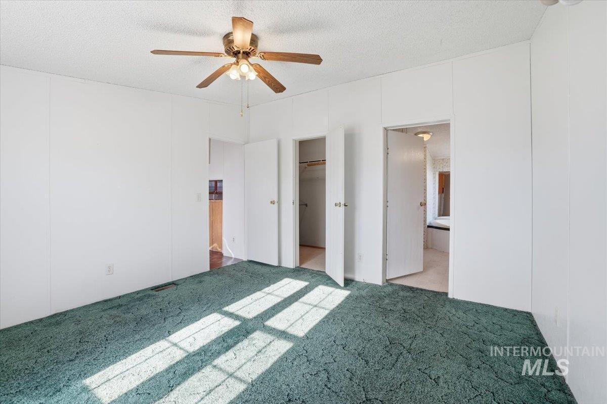 4320 West Pershall Road Marsing, ID 83639 - Photo 27 of 43 Unfurnished bedroom featuring carpet floors, a spacious closet, a ceiling fan, a textured ceiling, and connected bathroom