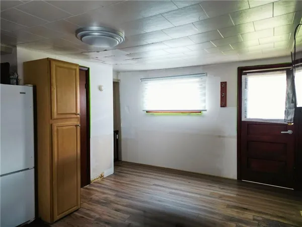 a view of an empty room with wooden floor and a refrigerator