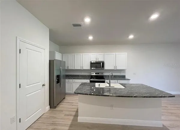 a kitchen with stainless steel appliances granite countertop a stove a refrigerator a sink a stove with white countertops and wooden floor