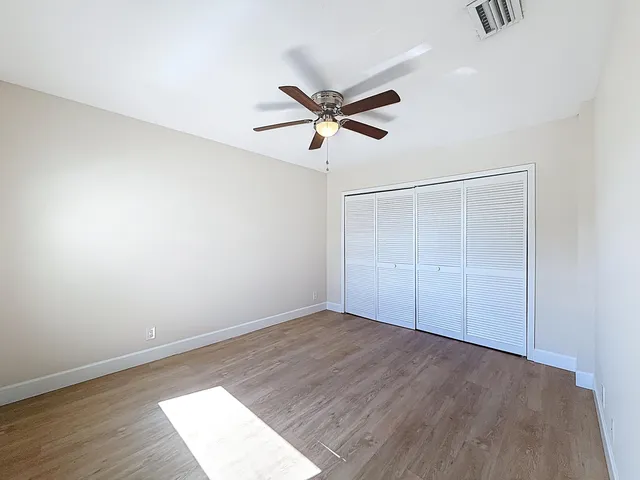 an empty room with wooden floor ceiling fan and windows