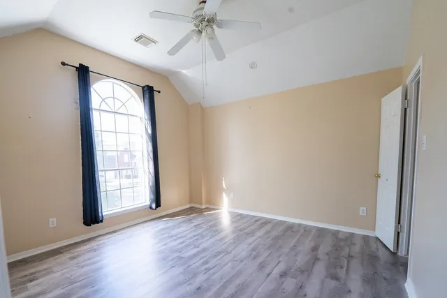 an empty room with wooden floor fan and windows