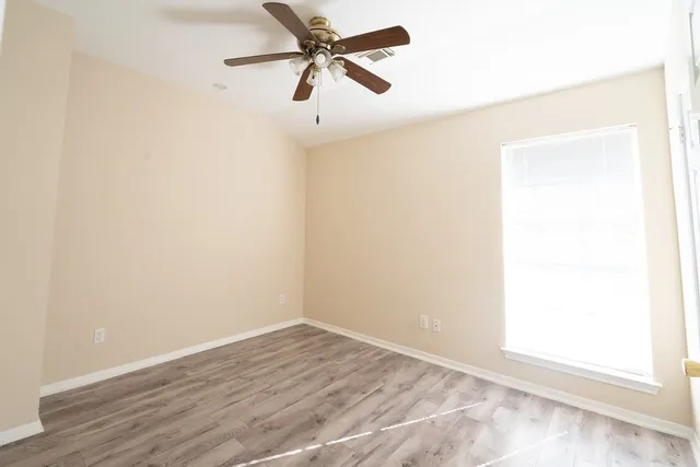 an empty room with wooden floor and fan