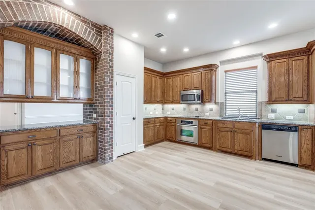 a large kitchen with stainless steel appliances kitchen island granite countertop a refrigerator a sink dishwasher a stove and white countertops with wooden floor