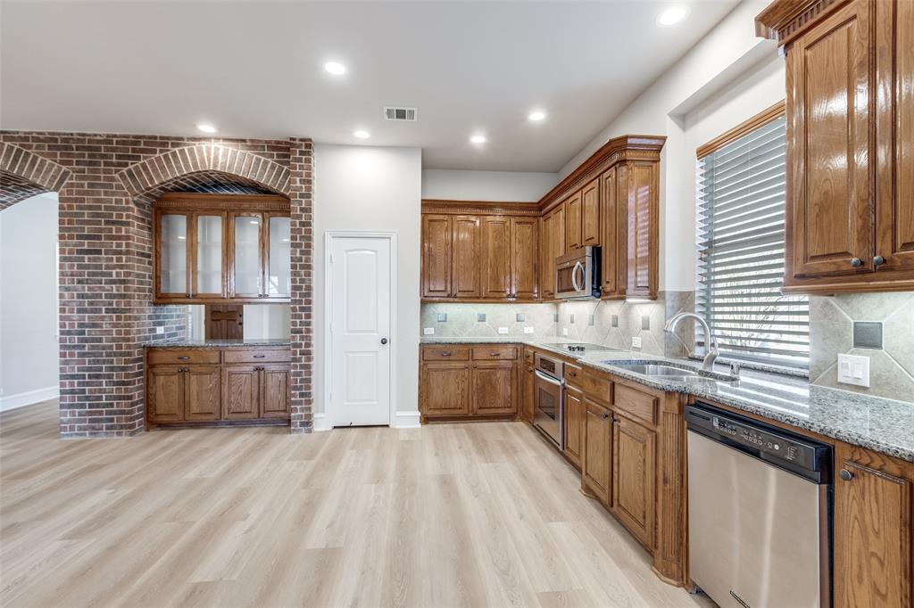 4009 Muscovy Drive McKinney, TX 75072 - Photo 10 of 31 a large kitchen with stainless steel appliances kitchen island granite countertop a refrigerator a sink dishwasher a stove and white countertops with wooden floor