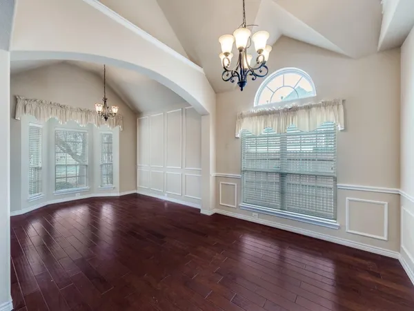 an empty room with wooden floor chandelier and windows