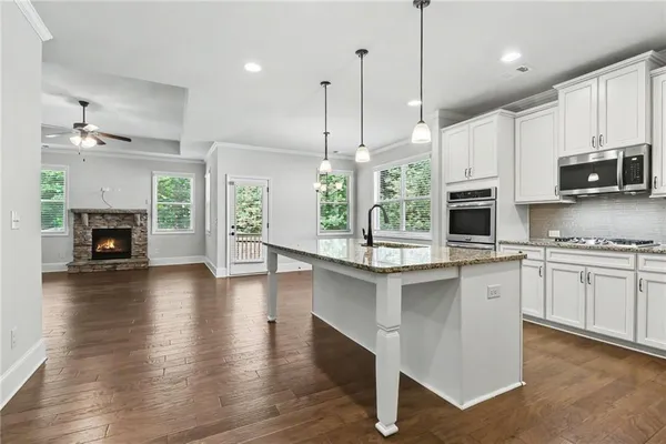a kitchen with stainless steel appliances granite countertop a refrigerator a stove a sink dishwasher and a fireplace with wooden floor