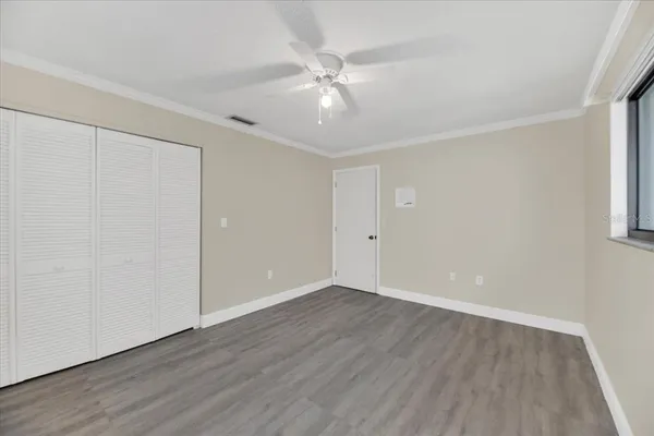 a view of an empty room with wooden floor and a ceiling fan