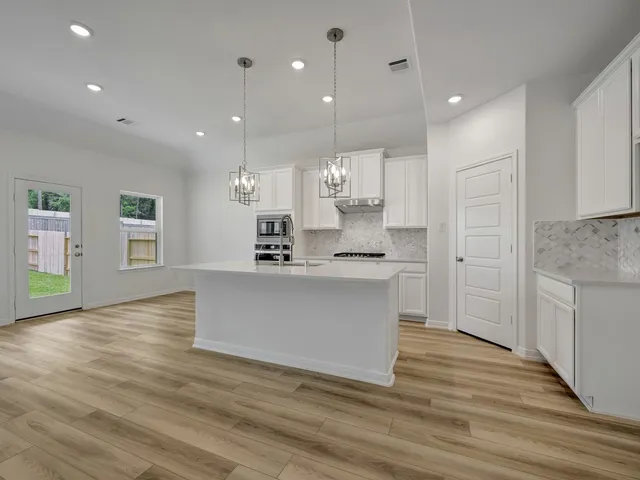 a large white kitchen with kitchen island a sink white cabinets and stainless steel appliances
