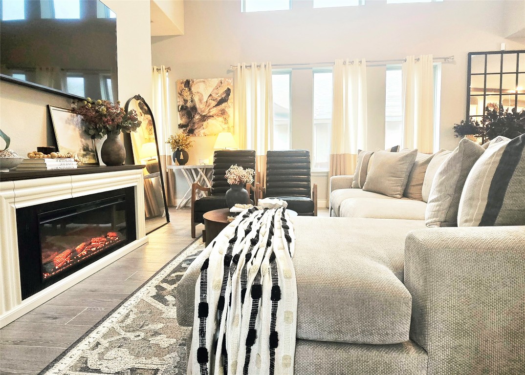Living room with wood look finished floors, a glass covered fireplace, a towering ceiling, and plenty of natural light