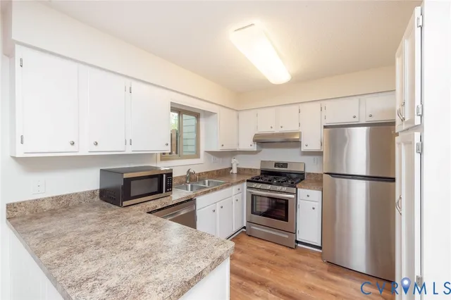 a kitchen with stainless steel appliances granite countertop a refrigerator a stove a sink and white cabinets