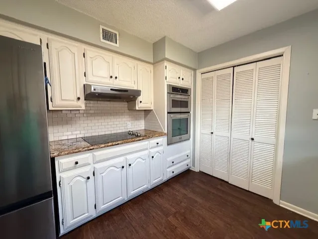 a kitchen with granite countertop white cabinets and stainless steel appliances