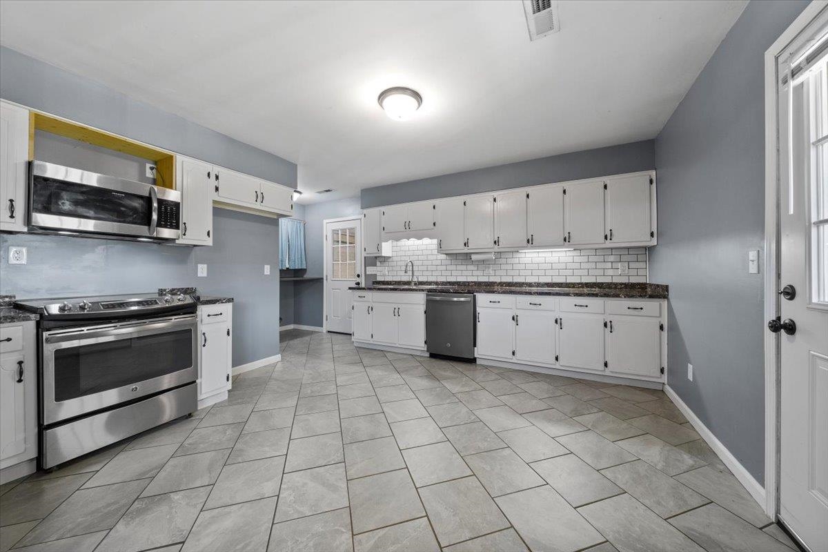 9496 Holly Grove Road Brighton, TN 38011 - Photo 11 of 29 Kitchen featuring stainless steel appliances, backsplash, white cabinets, light tile patterned flooring, and dark stone countertops