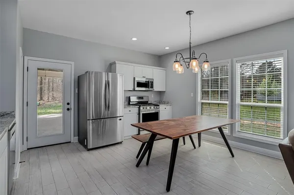 a kitchen with stainless steel appliances granite countertop a refrigerator a sink dishwasher a dining table and chairs with wooden floor