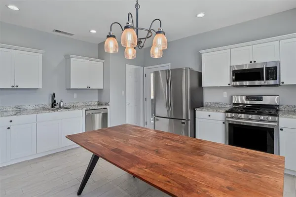 a kitchen with stainless steel appliances granite countertop a stove refrigerator a microwave oven a sink dishwasher and white cabinets with wooden floor