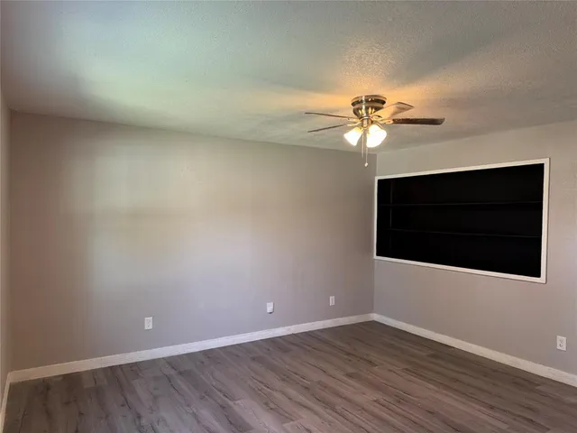 a view of an empty room with wooden floor and a ceiling fan