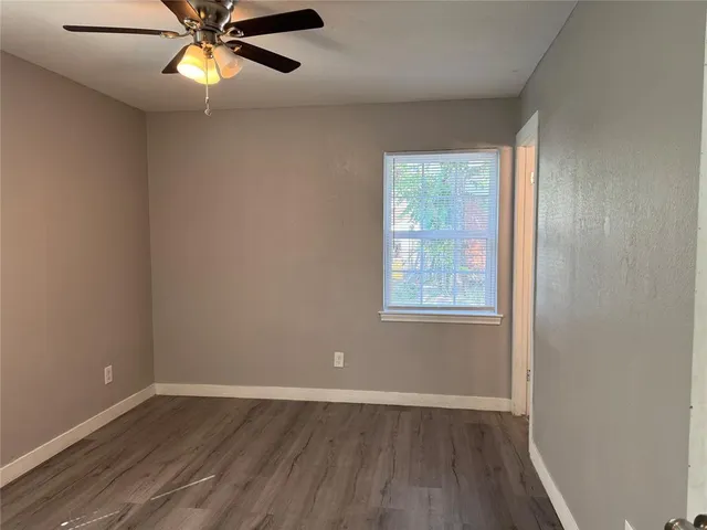 an empty room with wooden floor fan and windows