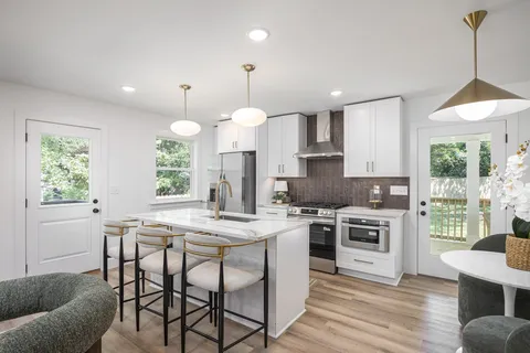 a kitchen with kitchen island granite countertop a stove a sink a dining table and chairs with wooden floor