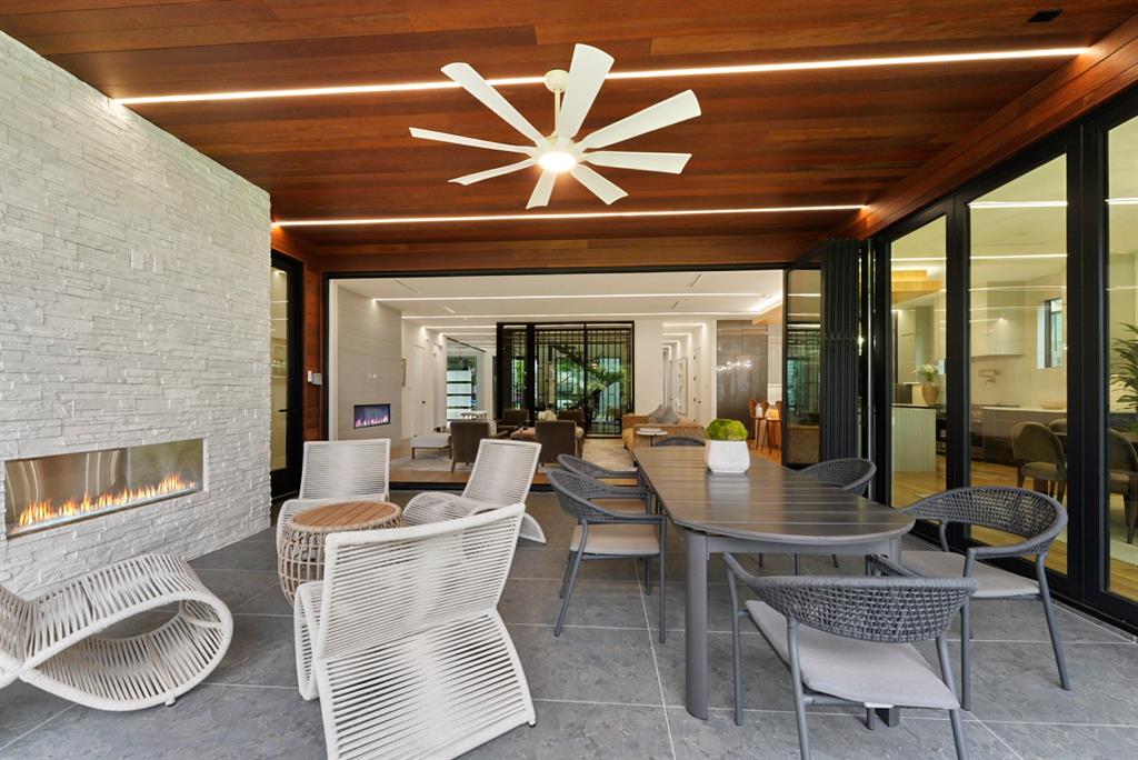 9457 Waterview Road Dallas, TX 75218 - Photo 12 of 25 Covered outdoor living area with a linear fireplace set into a stacked stone wall, wood-paneled ceiling with recessed lighting and ceiling fan, and large-format tile flooring